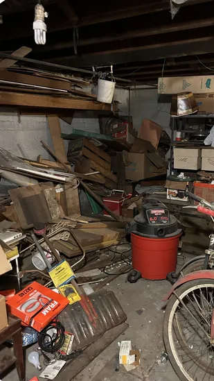 Vollgestellter Kellerraum mit Holz, Kartons, Fahrrad und Gerümpel vor der Entrümpelung