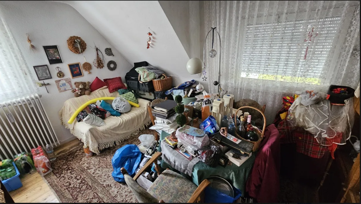 Vollgestelltes Dachgeschoss-Wohnzimmer mit Sofa, Taschen und Gerümpel vor der Haushaltsauflösung