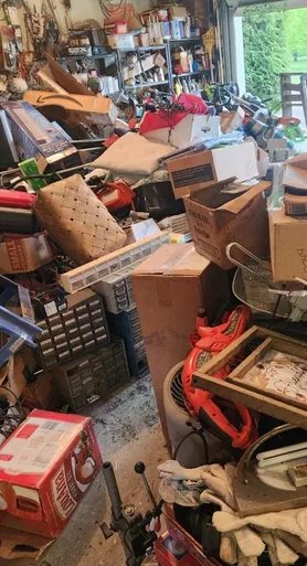 Vollgestellte Garage mit Regalen, Kartons, Fahrrad und Werkzeug vor der Entrümpelung